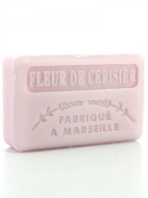 Jasnoróżowa tabliczka z wytłoczonymi napisami "FLEUR DE CERISIER" i "FABRIQUÉ À MARSEILLE" oraz małą ozdobną gałązką znajduje się na białym tle.