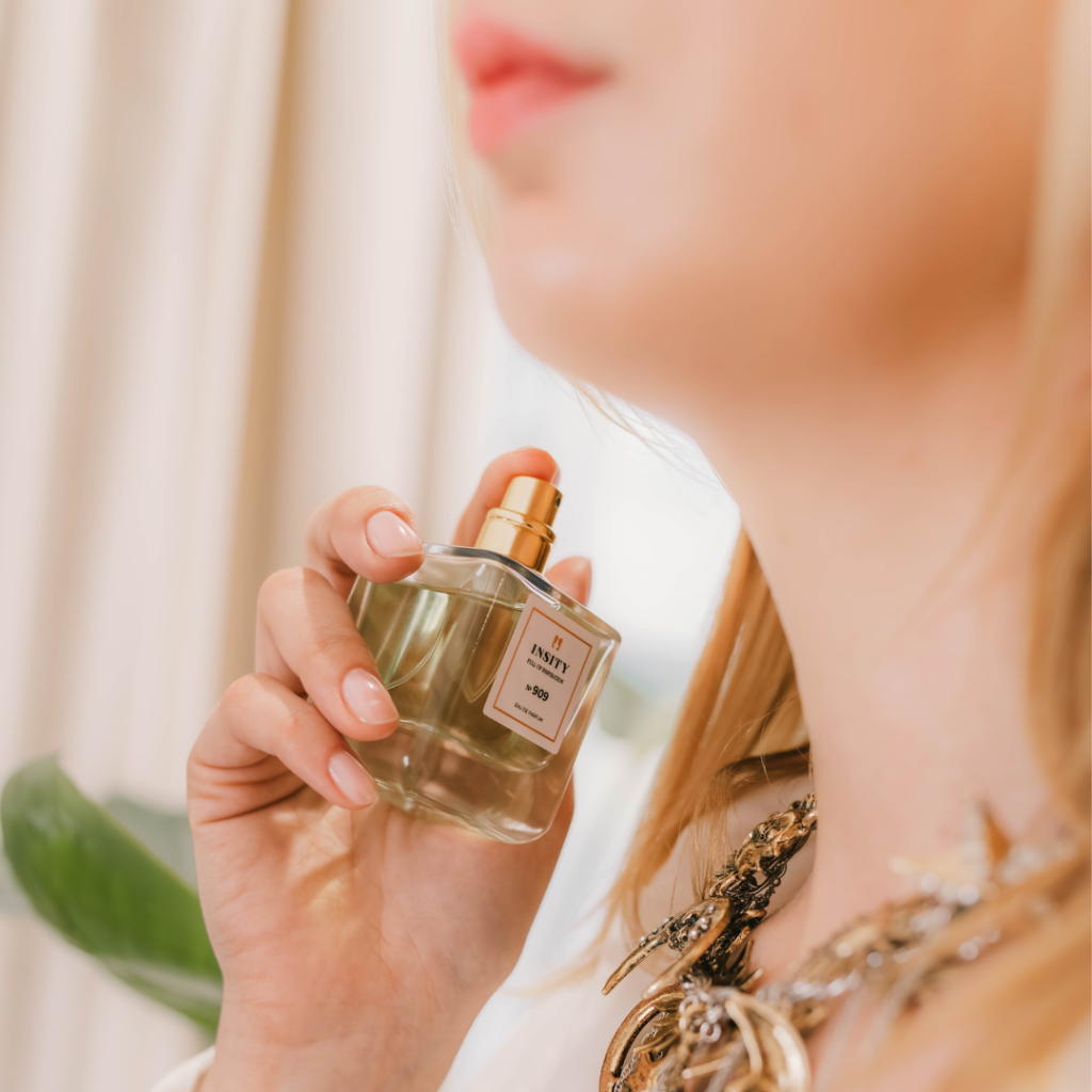 Kobieta trzyma przy szyi buteleczkę perfum Insity nr 909 (na mililitry).