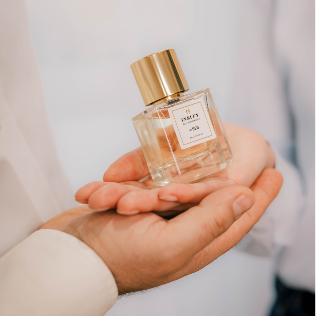 Dwie dłonie złożone w miseczkę, trzymające szklaną buteleczkę wody perfumowanej Insity nr 923, sprzedawaną jako perfumy na mililitry.
