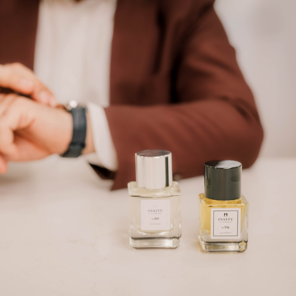 Dwie butelki perfum Insity (w mililitrach) stoją na stole przed osobą w brązowej marynarce, która spogląda na zegarek.