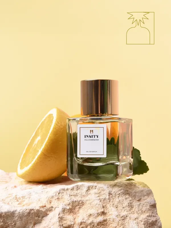 Butelka Perfumy Insity - Radość i zabawa spoczywa na kamieniu z połówką cytryny i zielonymi liśćmi, na żółtym tle z konturem owocu cytrusowego w prawym górnym rogu.